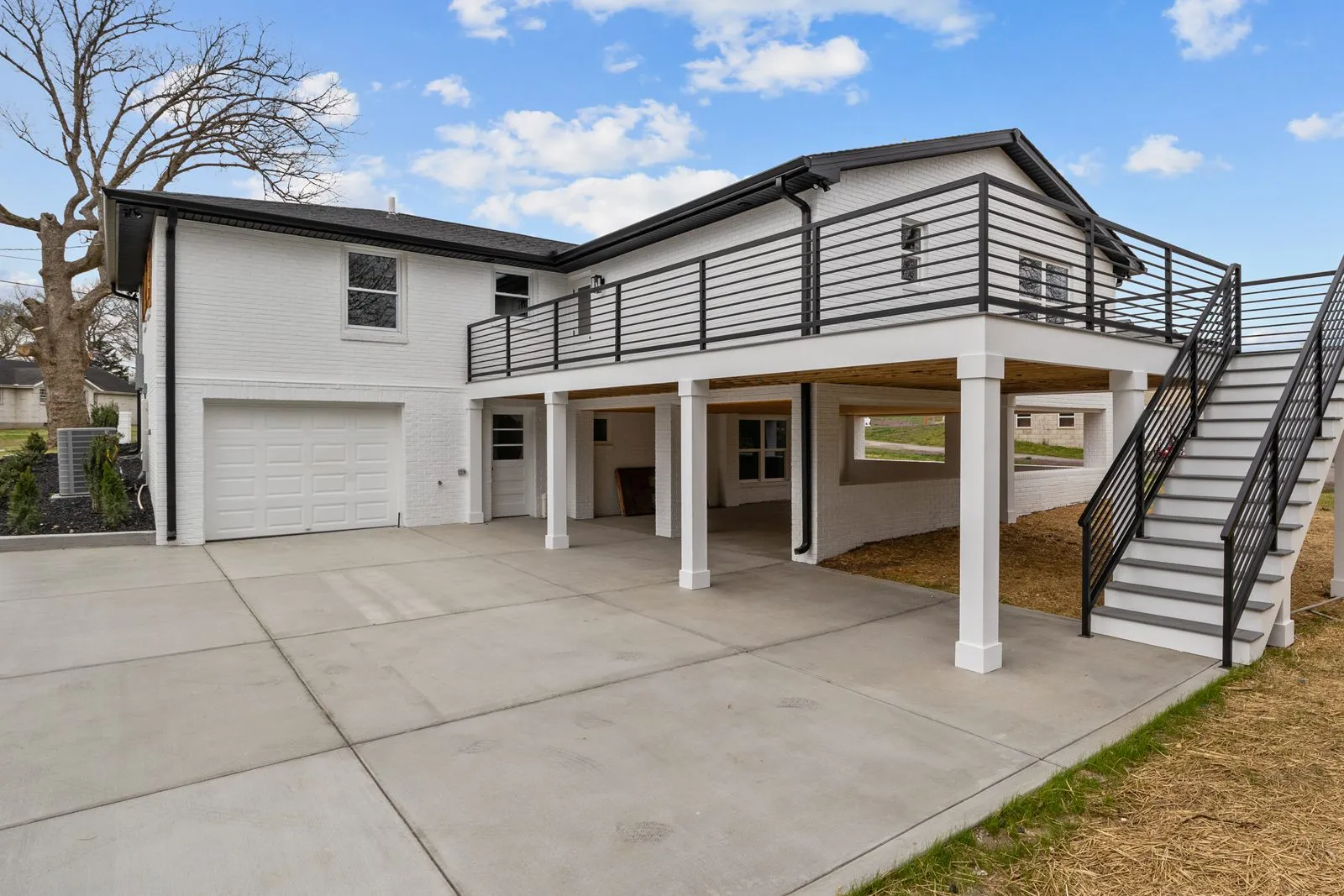 White brick house with a raised deck, black steel railings and stairs over a covered carport