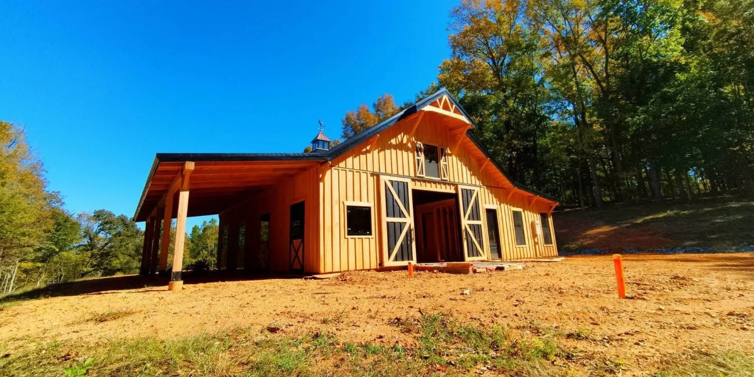 Wood board-and-batten barn with a cupola, black-and-white sliding doors and a covered lean-to