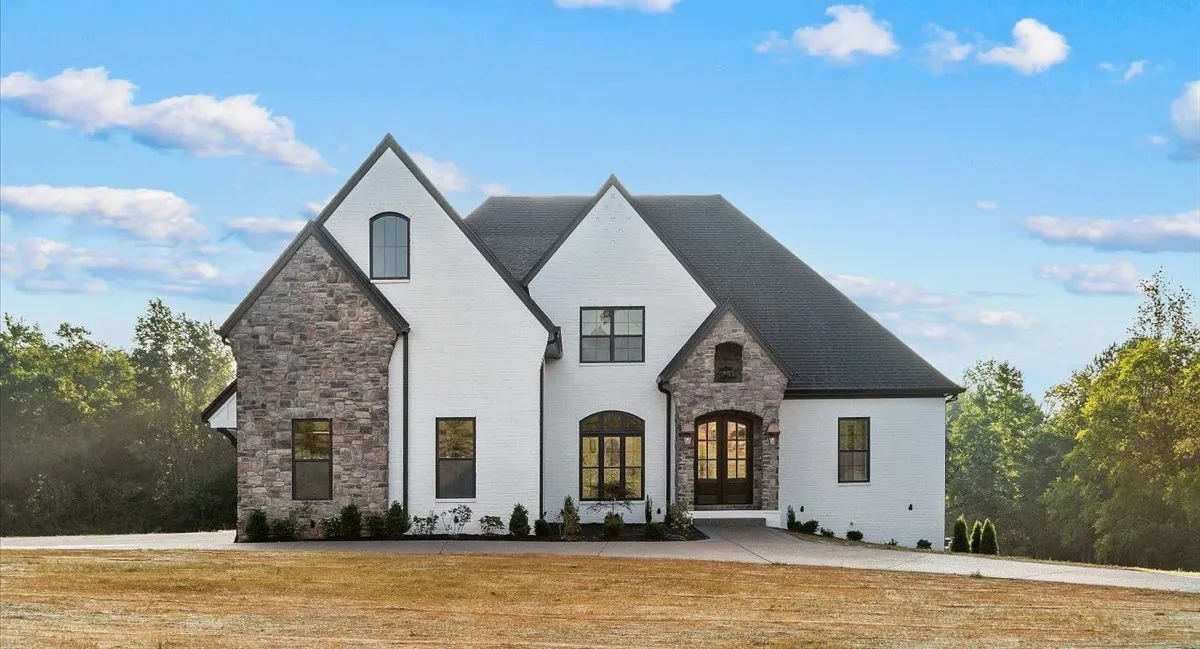 White brick and stone custom home with black windows, arched wood front doors and a dark shingle roof