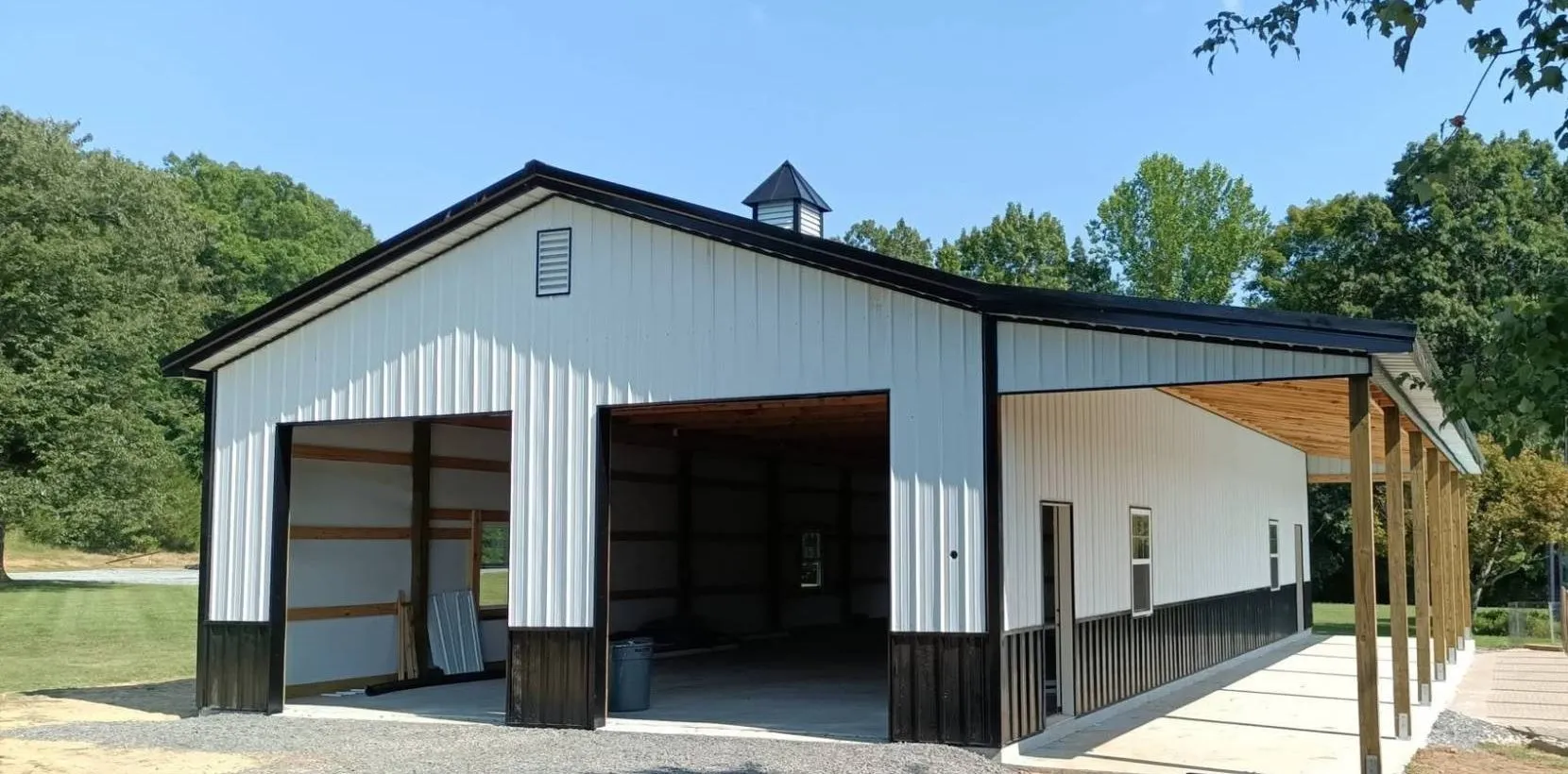 White metal post-frame shop with black trim, two open bays and a covered lean-to on posts