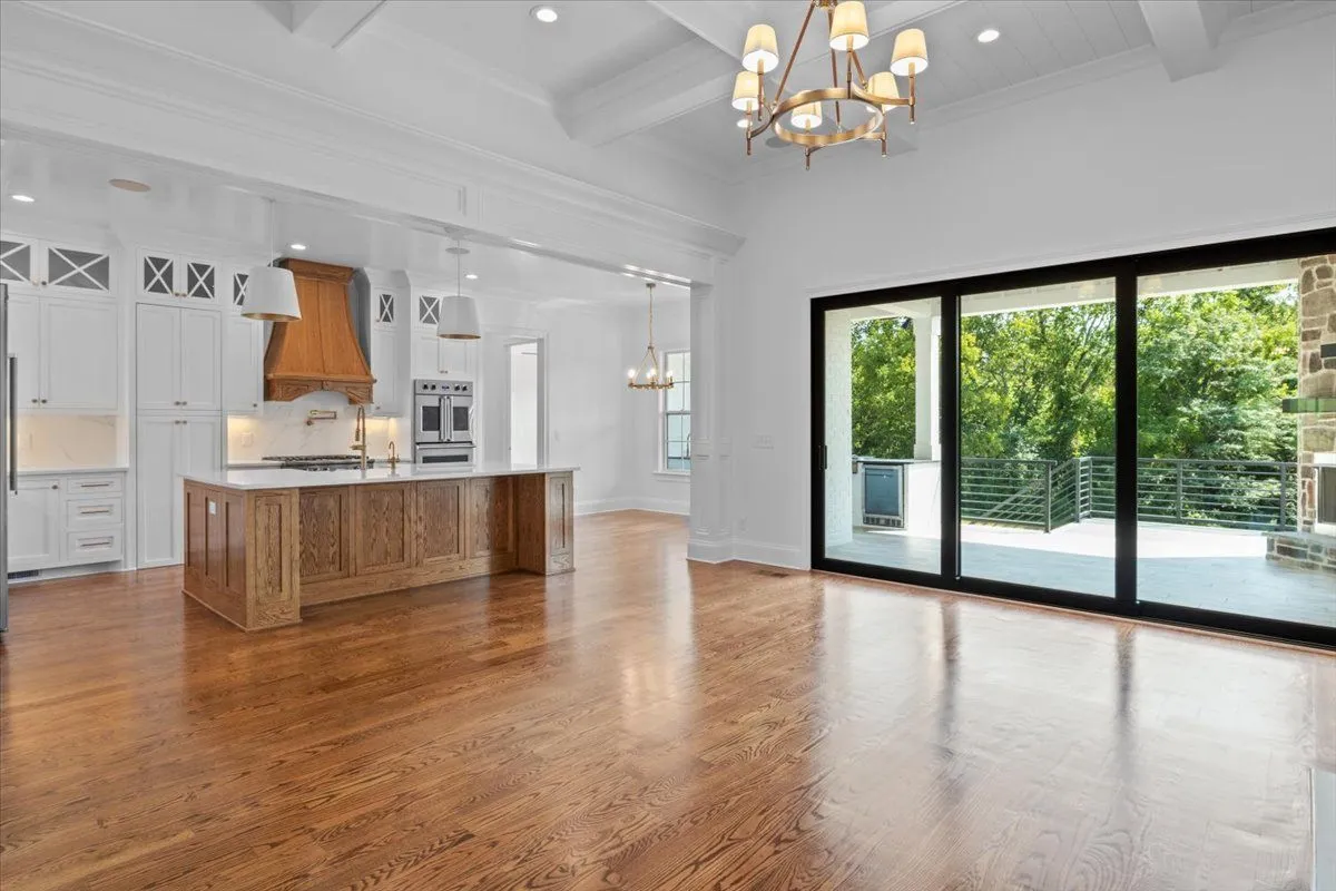 Open kitchen and living room: a wood island, a wood range hood, a brass chandelier and a wall of sliding glass doors to a covered deck