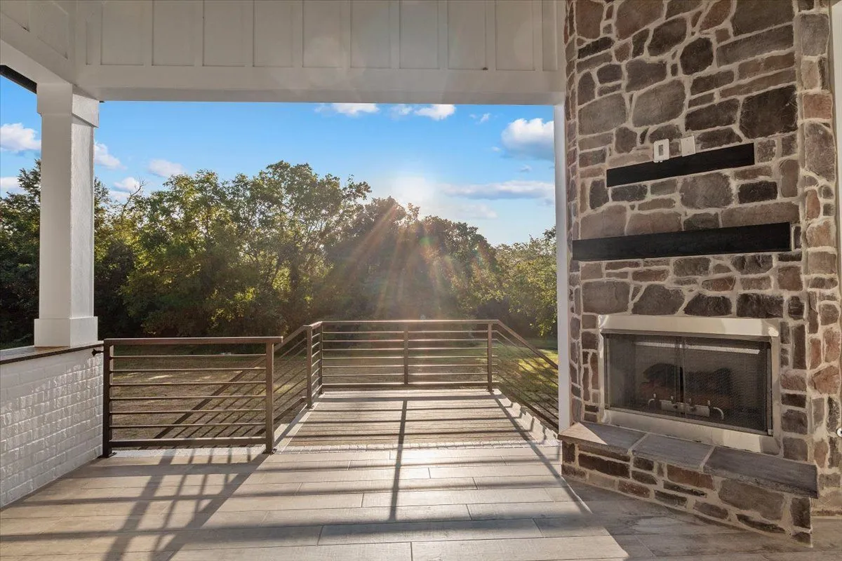 Covered back porch with a stone fireplace and steel railings, looking out over trees at sunset
