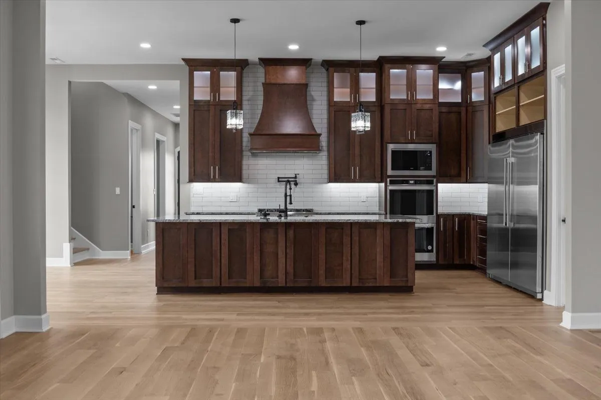 Kitchen with dark walnut-stained cabinets to the ceiling, a long island and a wood range hood