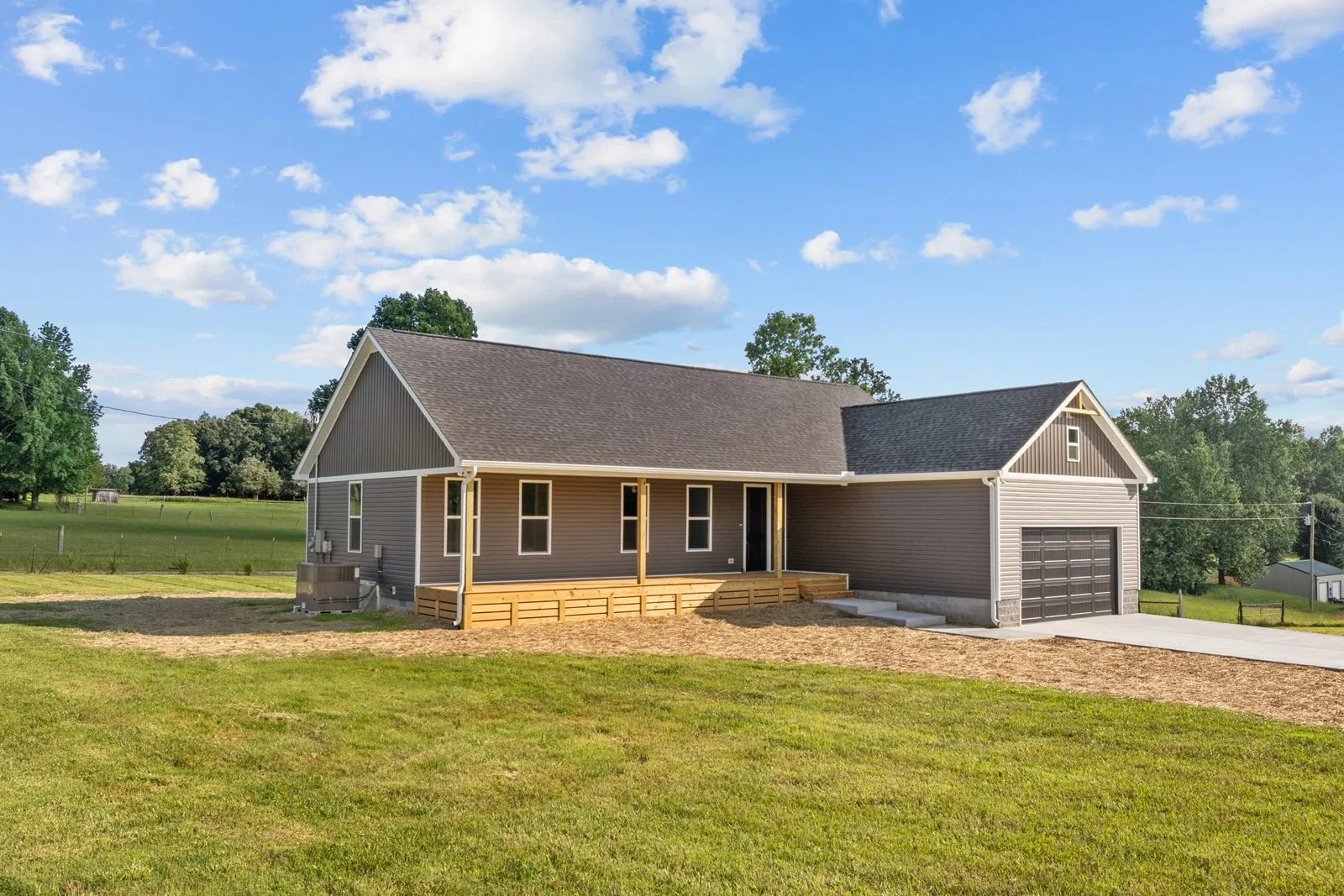 Gray ranch home with a wood front porch and a two-car garage on open pasture