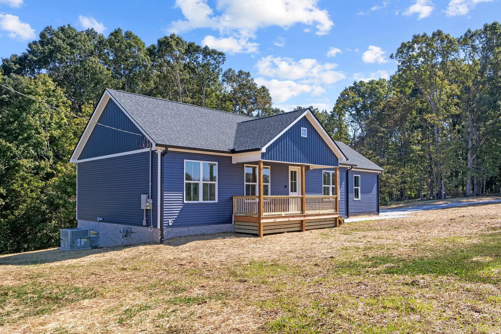 Blue ranch home with a wood front porch, set against a stand of trees
