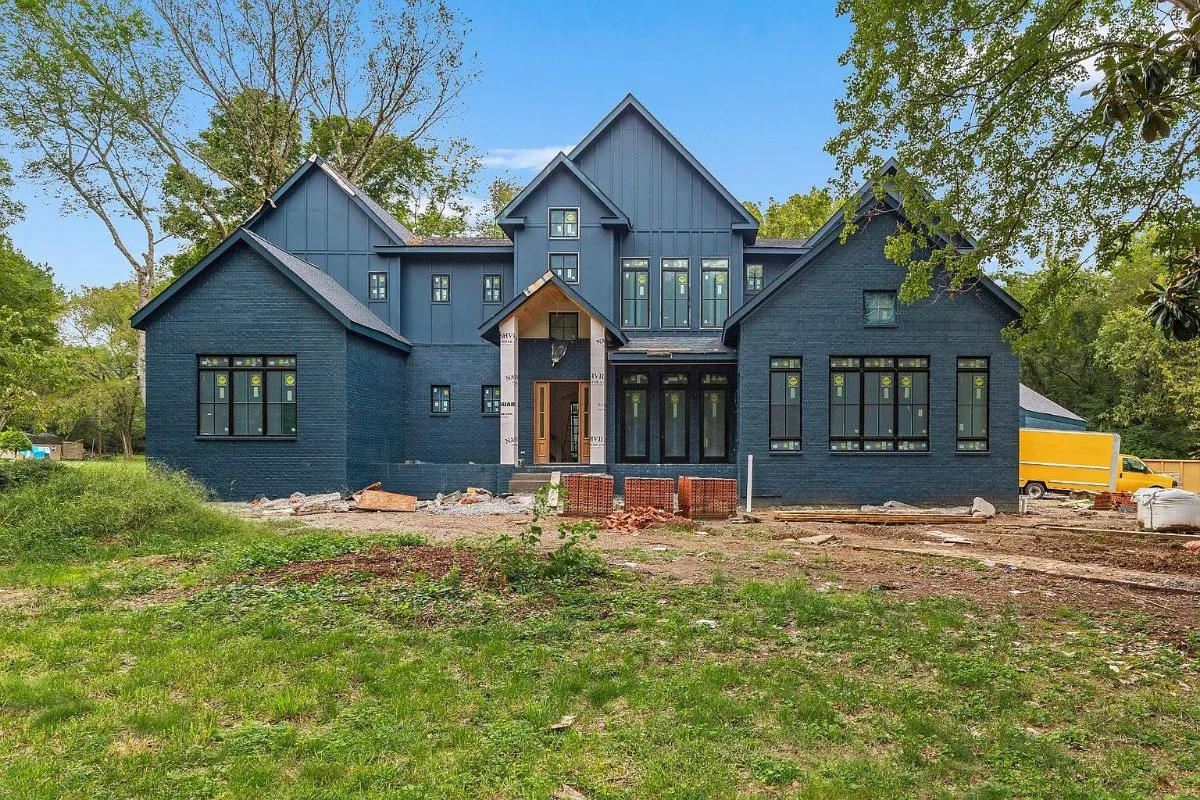 Front of the home during construction: navy board-and-batten siding and black windows, with site work still under way