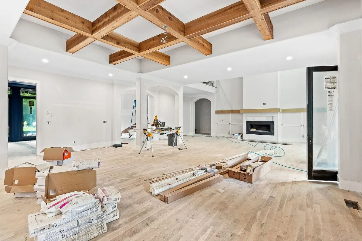 Great room under coffered wood beams during finishing, with flooring materials stacked
