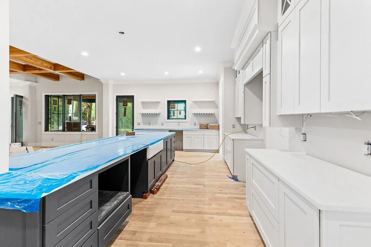 Kitchen during finishing: dark island and white cabinets, counters under protective film