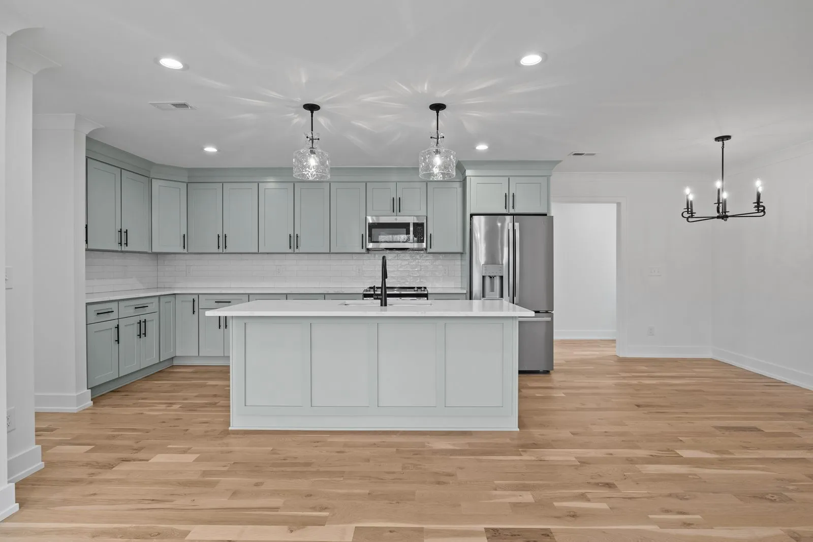 Kitchen with sage-green shaker cabinets, a white island, glass pendants and hardwood floors